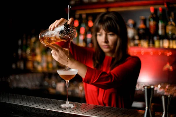 Wineglass stands on bar and bartender holds mixing cup and carefully pours drink into it — Stock Photo, Image