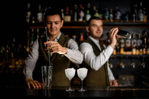 Vista de bar com copos cheios de gelo e bartenders masculinos preparando coquetel — Fotografia de Stock