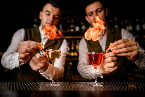 Glasses with drinks stands on bar and bartenders sprinkle and set them on fire — Stock Photo, Image