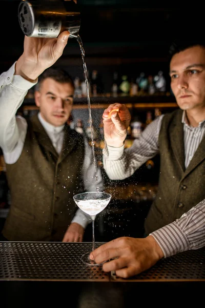 Homem barman derrama líquido em vidro de bebida e outro homem polvilha sobre ele — Fotografia de Stock