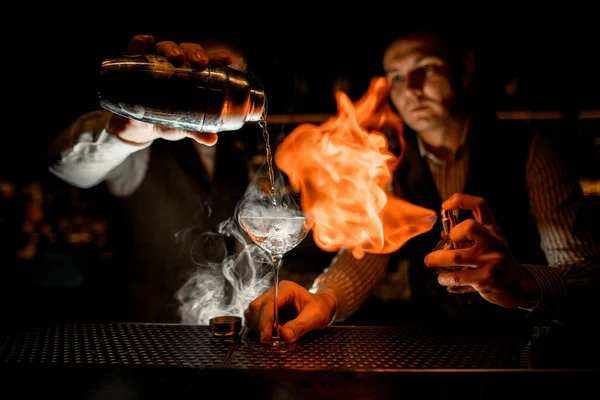 Muž nalije tekutinu do sklenice kouřícího nápoje a jiný muž ji pokropí a zapálí — Stock fotografie