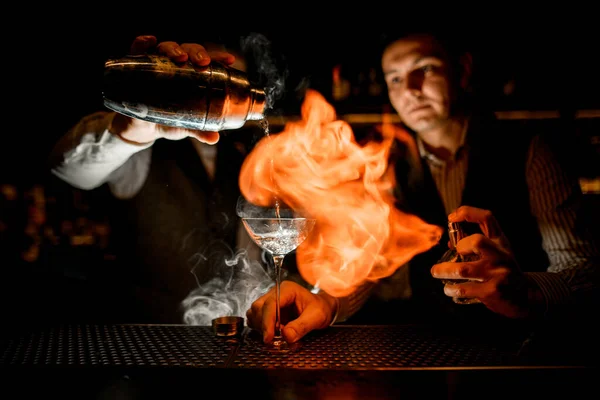 Barman pours drink into glass and another man sprinkles on it and sets fire — Stock Photo, Image