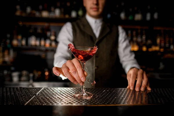 Belo vidro com bebida salpicante no bar e mão de homem barman segura — Fotografia de Stock