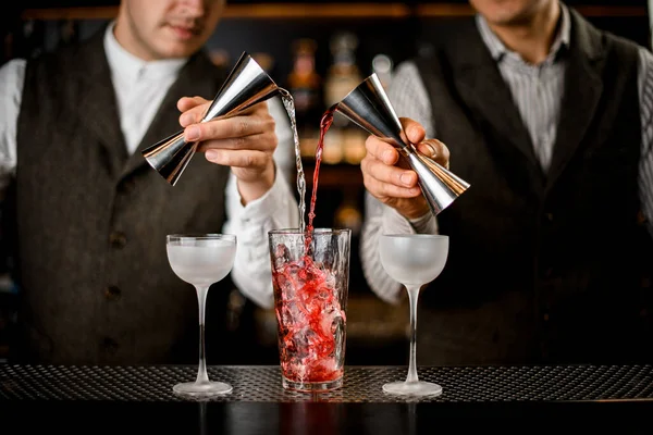 Bartenders segurar jiggers de aço e despeje cuidadosamente bebida em vidro com cubos de gelo — Fotografia de Stock