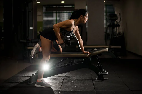 Sidovy av muskulös kvinna som tränar i gym med hantel i handen på simulator. — Stockfoto
