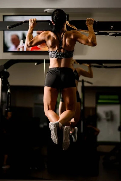 Rückansicht starker muskulöser Körper einer Frau, die Klimmzüge im Fitnessstudio macht. — Stockfoto
