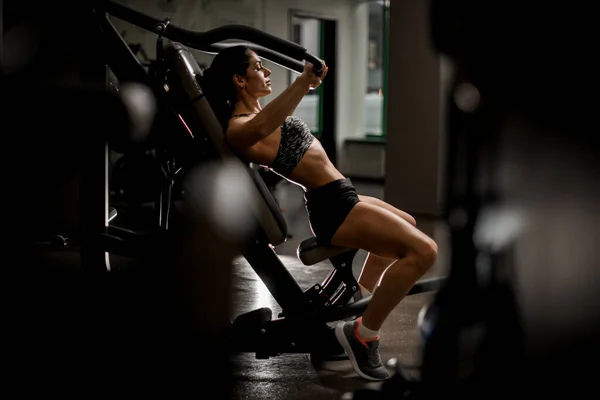 Gezicht van een sportieve vrouw die oefeningen doet op de simulator in een fitnessclub. — Stockfoto