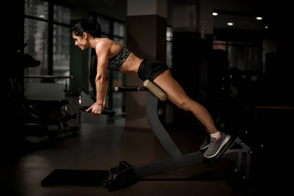 Oldalnézet vonzó barna nő edz a szimulátor az edzőteremben. — Stock Fotó