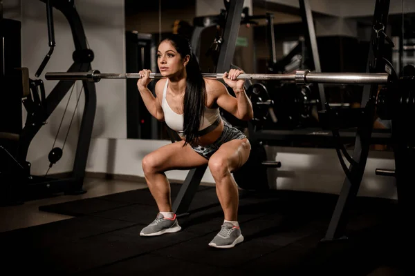 Attraktiv stark muskulös kvinna kroppsbyggare med skivstång gör knäböj i gymmet. — Stockfoto