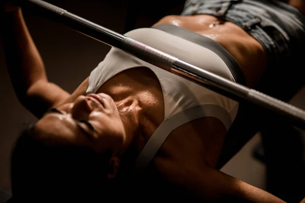 Close-up van de vrouw verhoogt lange halter liggend op de bank op de simulator in de sportschool. — Stockfoto