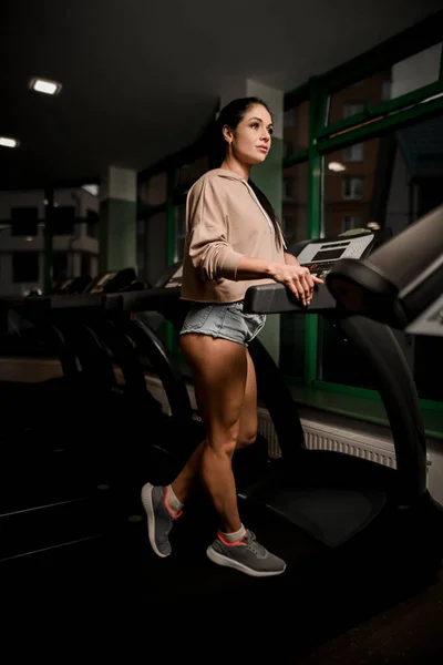 Vacker sportig brunett kvinna står på löpband i gymmet — Stockfoto