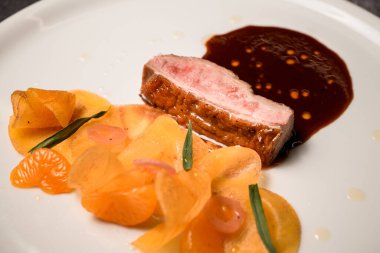 Tabağa yakından bak. Bir parça et, sos ve mandalina dilimleri..