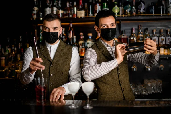 bartenders with masks on their faces preparing cocktails at the bar