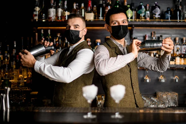 Camareros masculinos se encuentra lado a lado en el bar y mezclar cóctel en cocteleras — Foto de Stock