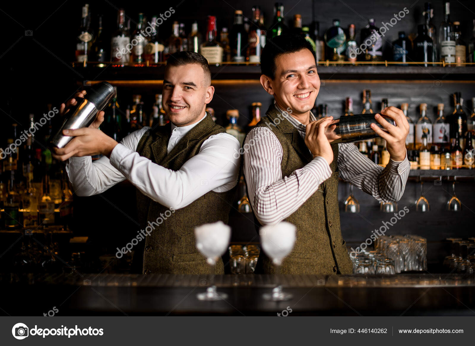 Happy men bartenders stands side by side at bar and stir cocktail in