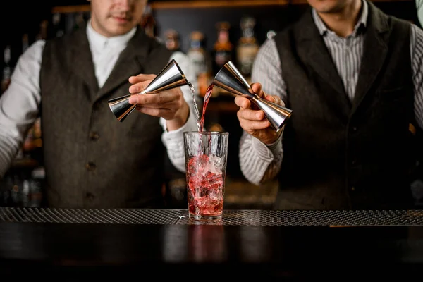 Bartenders segurar jiggers de aço e despeje bebida em vidro com cubos de gelo — Fotografia de Stock