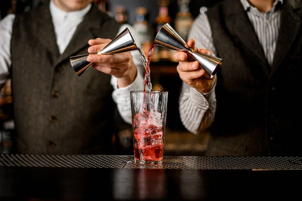 Bartenders segurar jiggers de aço e precisa derramar bebida em vidro com cubos de gelo — Fotografia de Stock