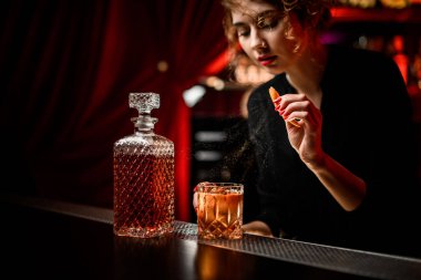 Bayan barmen bardaklara dikkatli bir şekilde alkollü kokteyl serpiyor.