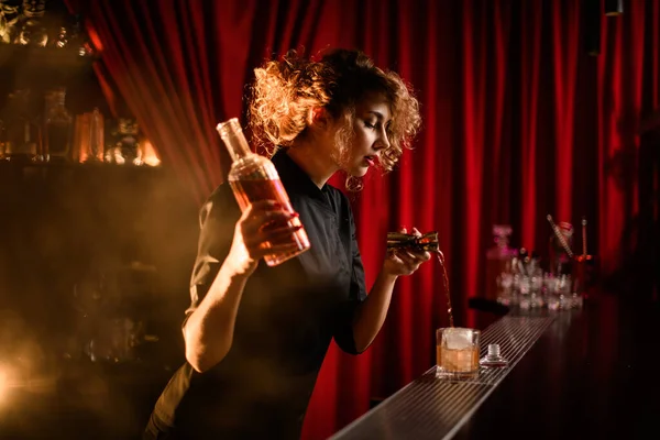 Барменша с бутылкой ликера в руке и наливает напиток из стакана в стакан — стоковое фото