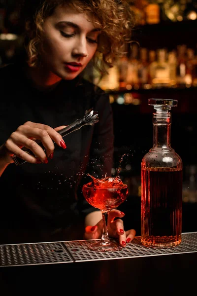 Beautiful woman bartender adds ice cube to the glass with cocktail — Stock Photo, Image