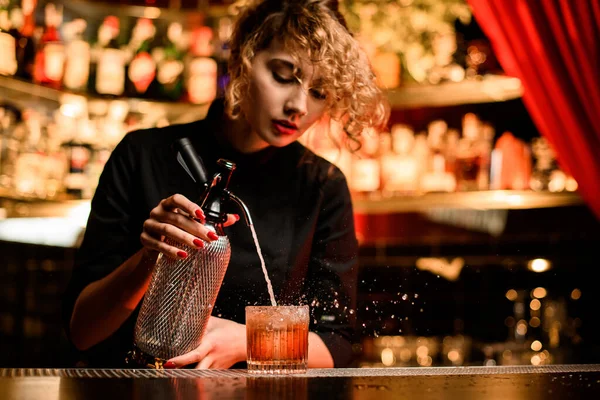 Atraktivní barmanka stojí za barem a nalévá nápoj ze sifonu do skla — Stock fotografie
