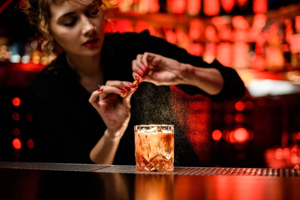 Woman bartender gently sprinkles on glass with cold alcoholic cocktail on the bar counter — Stock Photo, Image