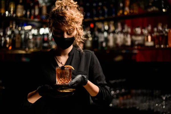 Вид женщины в черной маске и черных перчатках, держащей стакан с коктейлем — стоковое фото
