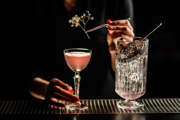 Close-up of glass with pink alcoholic drink which woman decorates with sprig of white flower — Stock Photo, Image