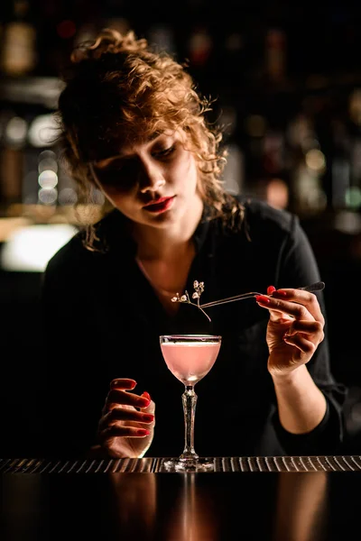 Aantrekkelijke vrouw barman netjes versiert glas met cocktail met bloem takje met pincet — Stockfoto