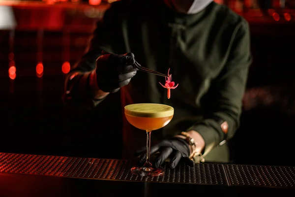 Hand van barman houdt bloem met pincet en versiert glas cocktail mee — Stockfoto