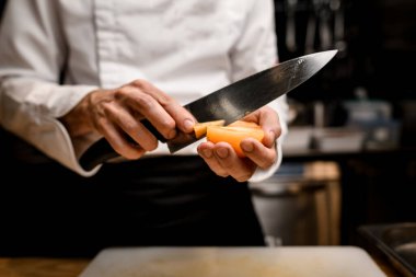 Şef 'in elindeki sarı domatesin yakın plan görüntüsü bıçakla kesiliyor.