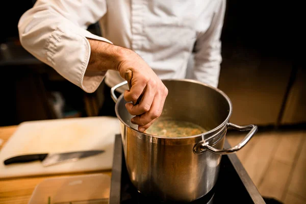 Close-up on the hand of male chef who is stirring soup in pot with spoon — Stock Photo, Image