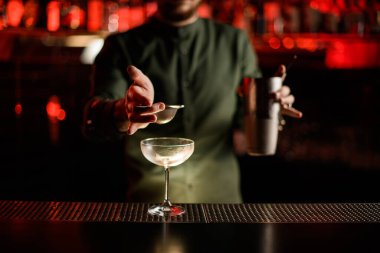 Barın tezgahında boş bardaklar duruyor ve barmenin eli onun üzerinde elek tutuyor.