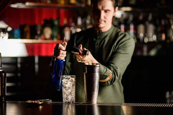 Jovem barman masculino gentilmente derrama bebida jigger em vidro de aço de agitador. — Fotografia de Stock