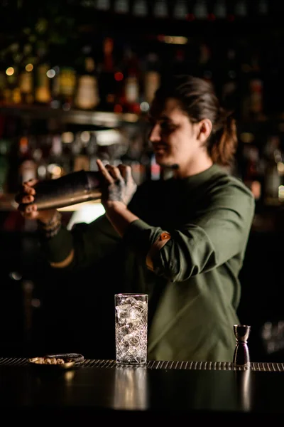 Vidrio transparente con hielo y soporte de jigger en barra de bar. Barman borroso de fondo — Foto de Stock