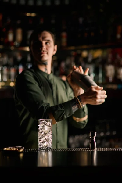 Hermoso vaso con hielo y jigger stand en barra de bar. Barman borroso de fondo — Foto de Stock