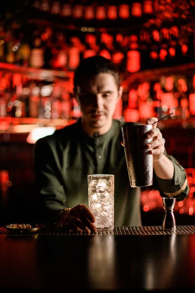 Glas met ijsblokjes op de bar en de barman gaat cocktail inschenken — Stockfoto