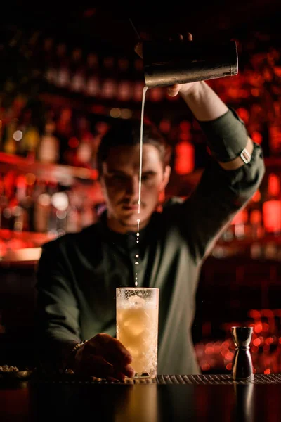 Barman profesional vierte suavemente cóctel de coctelera en vidrio en el mostrador de bar — Foto de Stock