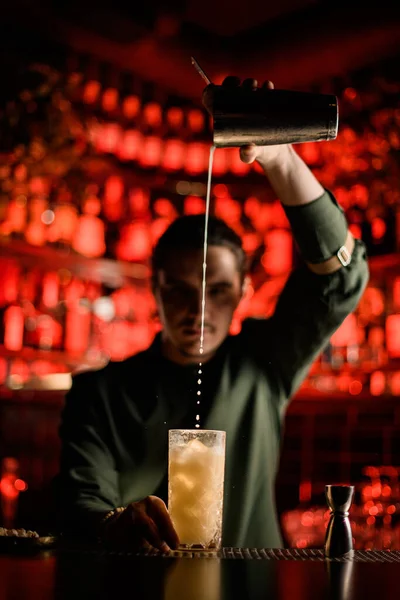 Camarero masculino vierte suavemente cóctel de coctelera en vidrio en el mostrador de la barra — Foto de Stock
