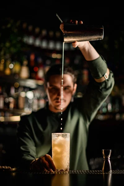 Bartender suavemente derrama coquetel de shaker em vidro no balcão do bar — Fotografia de Stock