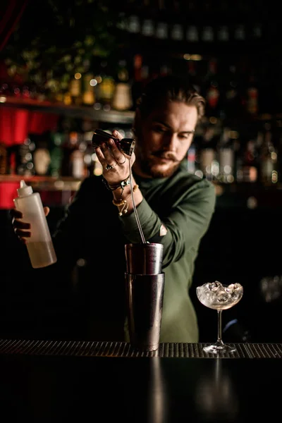 Man bartender skickligt häller sprit från jigger i stål skakkopp på bardisk — Stockfoto