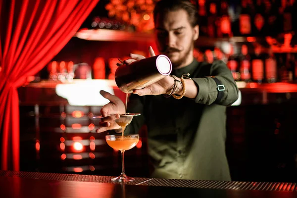 Mannelijke barman schenkt cocktail van shaker filteren door zeef in glas — Stockfoto
