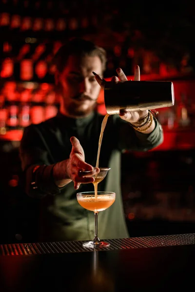 Camarero hombre hábilmente vierte cóctel de coctelera filtrando a través de tamiz en vidrio — Foto de Stock