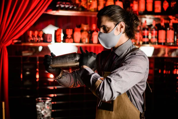 Вид человека бармена в фартуке и маске и перчатки со стальным шейкером — стоковое фото