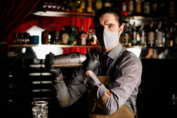 Вид бармена в фартуке и маске и перчатках со стальным шейкером — стоковое фото