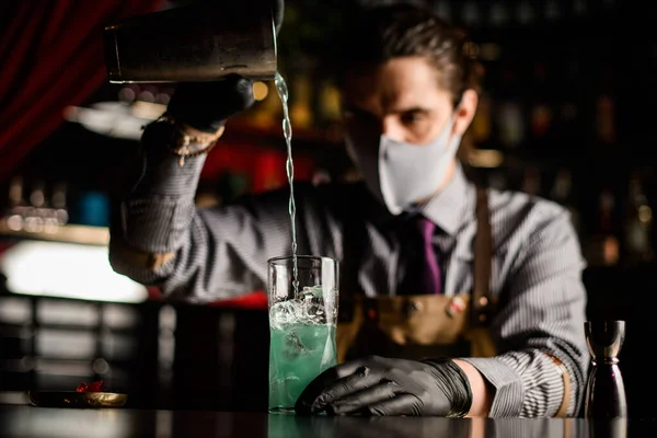 Крупным планом стекла с кубиками льда, в который бармен наливает синий коктейль из шейкера — стоковое фото