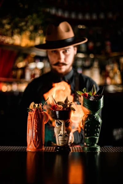 Varias copas de cóctel en el mostrador del bar y el camarero hombre los prende fuego —  Fotos de Stock
