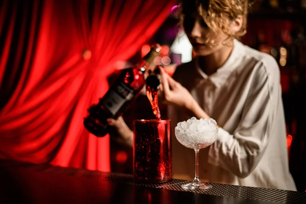 Handsome woman bartender professionally pours drink from jigger into large cup. — Stock Photo, Image