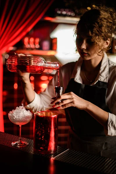 Young beautiful woman bartender pours drink from crystal bottle into jigger. — Stock Photo, Image