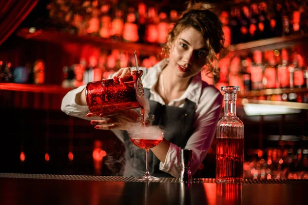 Pretty woman bartender pouring bright steaming cocktail into glass on bar counter — Stock Photo, Image